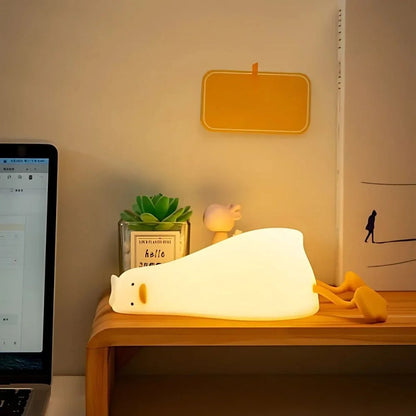 Lazy Duck night light lying on a desk beside a small plant — Casa Norex
