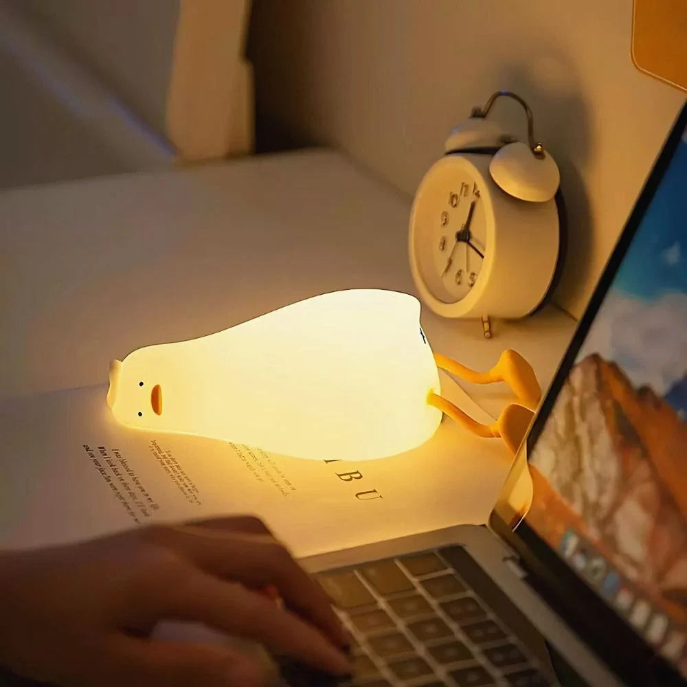 Lazy Duck night light lying on a desk beside a laptop and alarm clock — Casa Norex