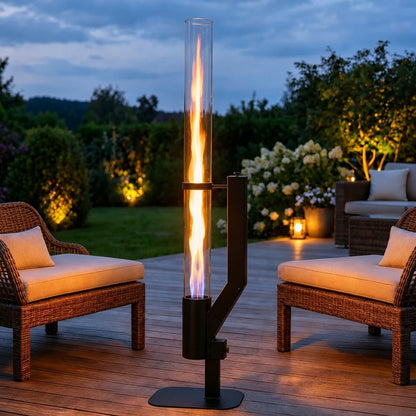 Outdoor pellet torch — tall glass flame chamber on a black base beside patio sofas | Casa Norex