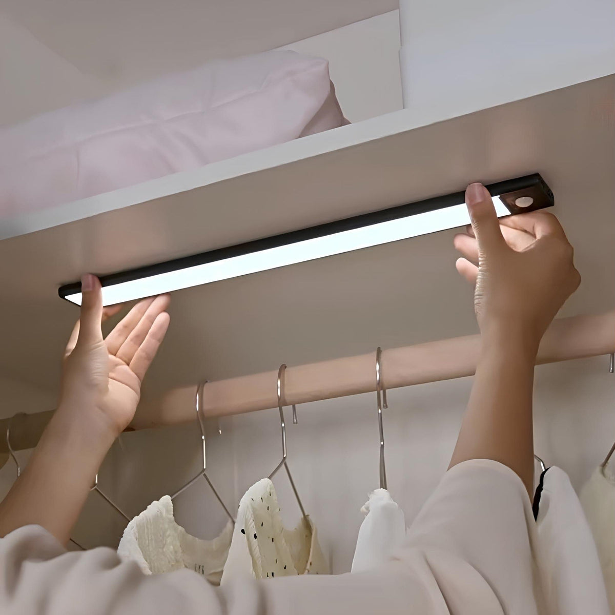 Hands attaching a light bar to a closet rail above hanging clothes — Casa Norex