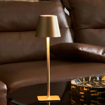 Gold table lamp lit warmly in front of a brown leather sofa — Casa Norex