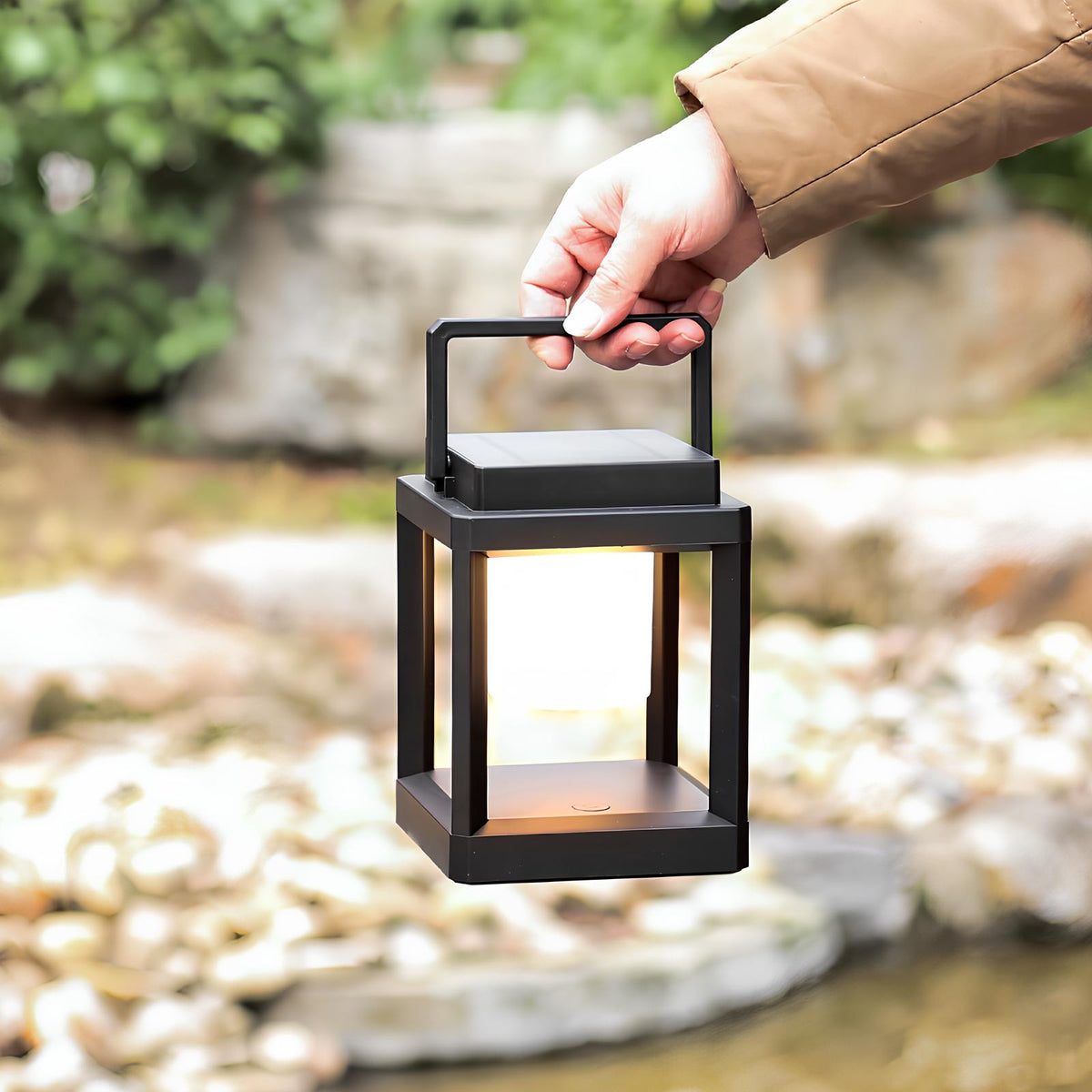 Hand carrying a portable lantern by its handle beside a stream — Casa Norex