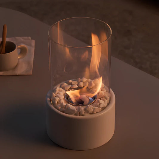 White tabletop oil lamp with a flame above decorative stones in a glass cylinder | Casa Norex