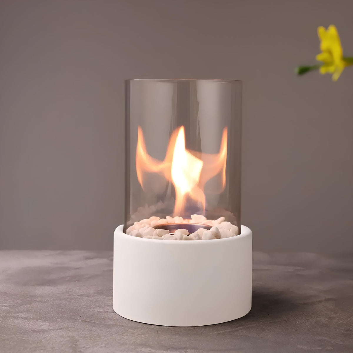 White oil lamp with a warm flame beside a yellow flower — Casa Norex