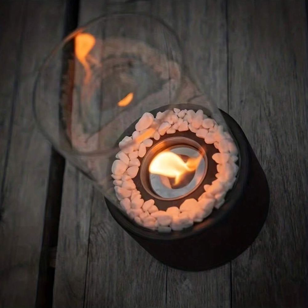 Top-down view of a flame ringed by decorative stones on a dark wooden surface — Casa Norex