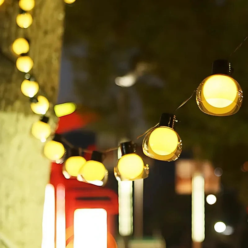 Globe string lights glowing beside a red lantern at night — Casa Norex