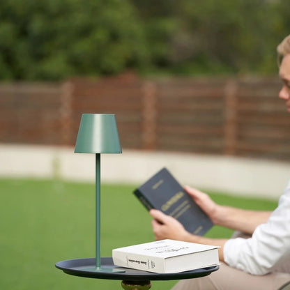 Matte green table lamp on a garden table with a person reading — Casa Norex