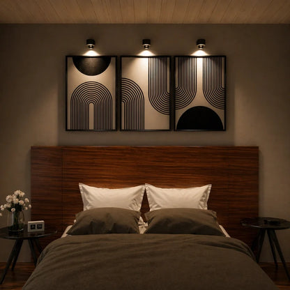 Three cordless wall lamps above framed art over a bed — Casa Norex
