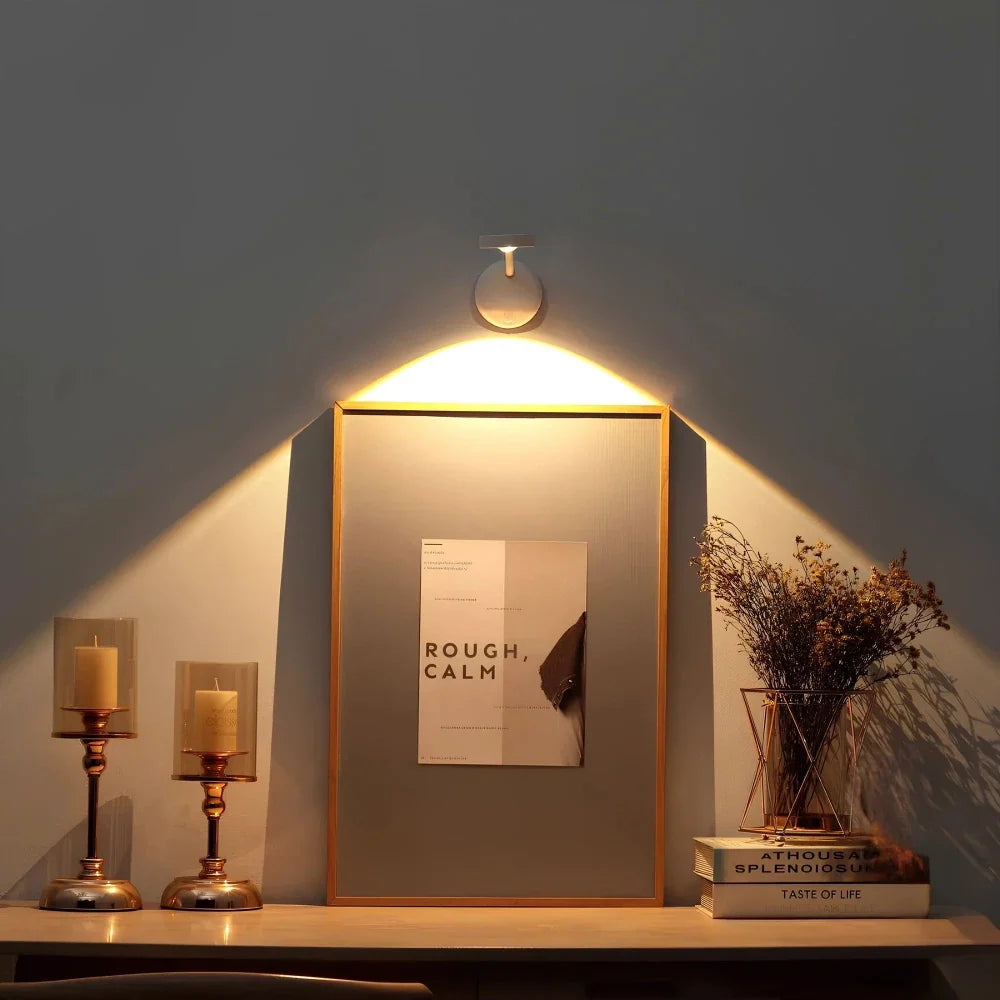 Round wall spotlight above a framed print on a console beside candlesticks | Casa Norex