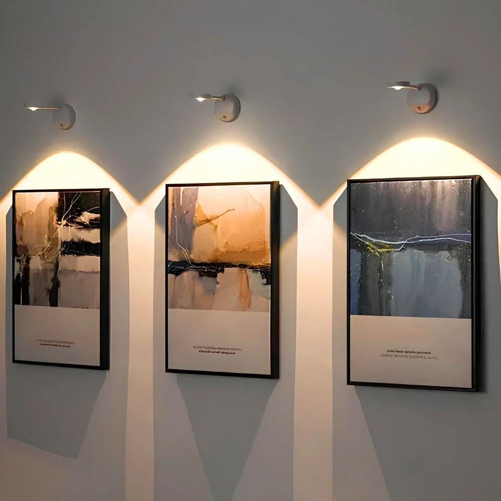 Three white spotlights above framed paintings on a gray wall | Casa Norex