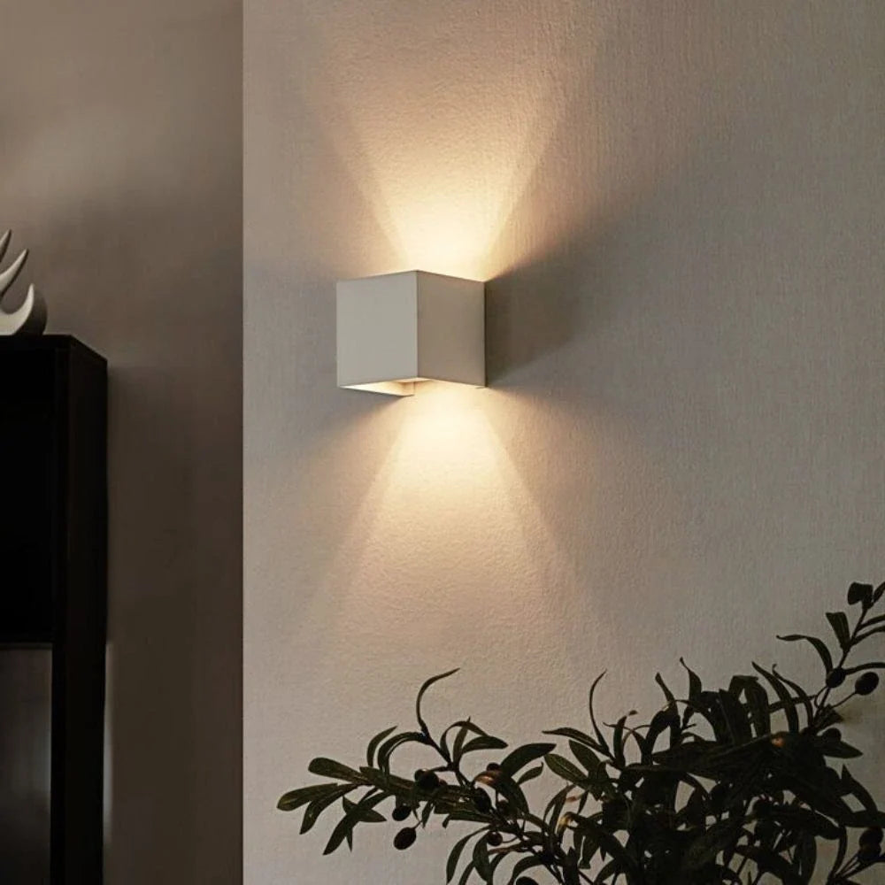 White cube wall light beside a leafy plant on a gray wall — Casa Norex