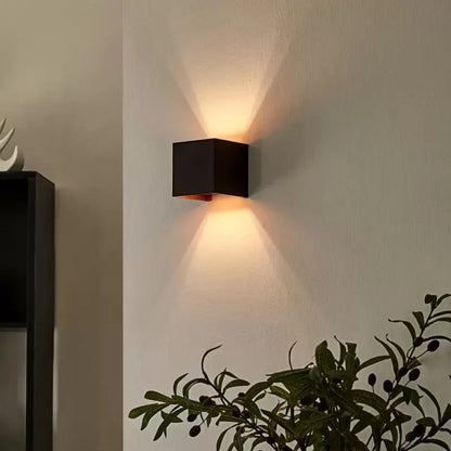 Black cube wall light with warm orange light beside a plant — Casa Norex