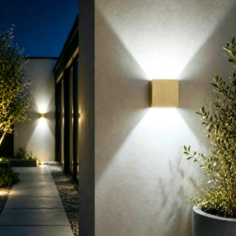 Brushed gold cube wall light beside a pathway at night — Casa Norex