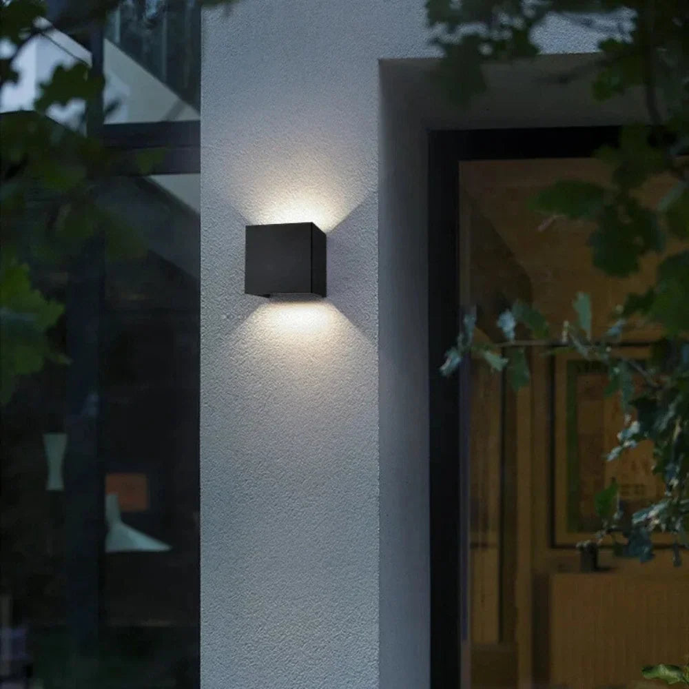 Black cube wall light beside a glass door and greenery — Casa Norex