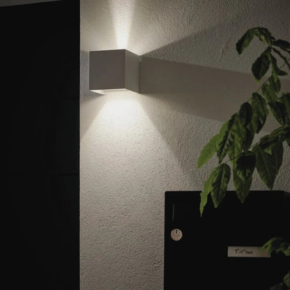 White cube wall light beside a dark door and plant — Casa Norex