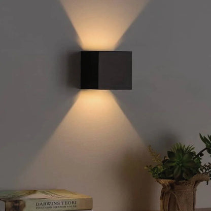 Black cube wall light over a side table with books and a plant — Casa Norex
