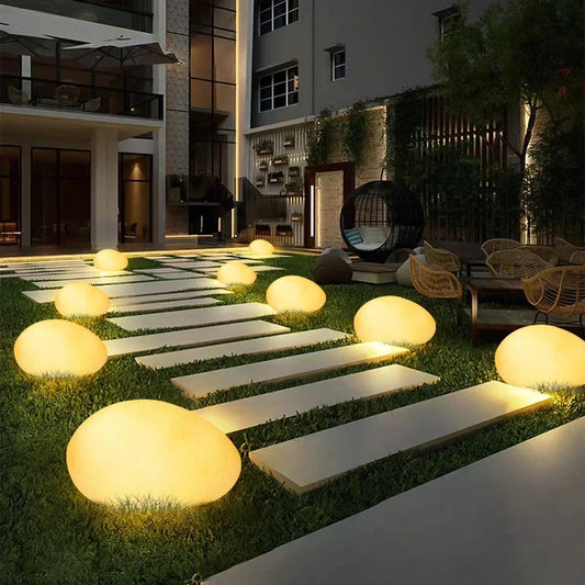 Glowing stone garden light beside stepping stones in a landscaped garden | Casa Norex