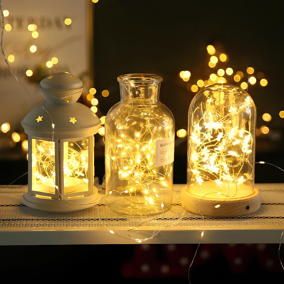 Warm white fairy lights glowing inside glass bottles and lanterns on a shelf — Casa Norex