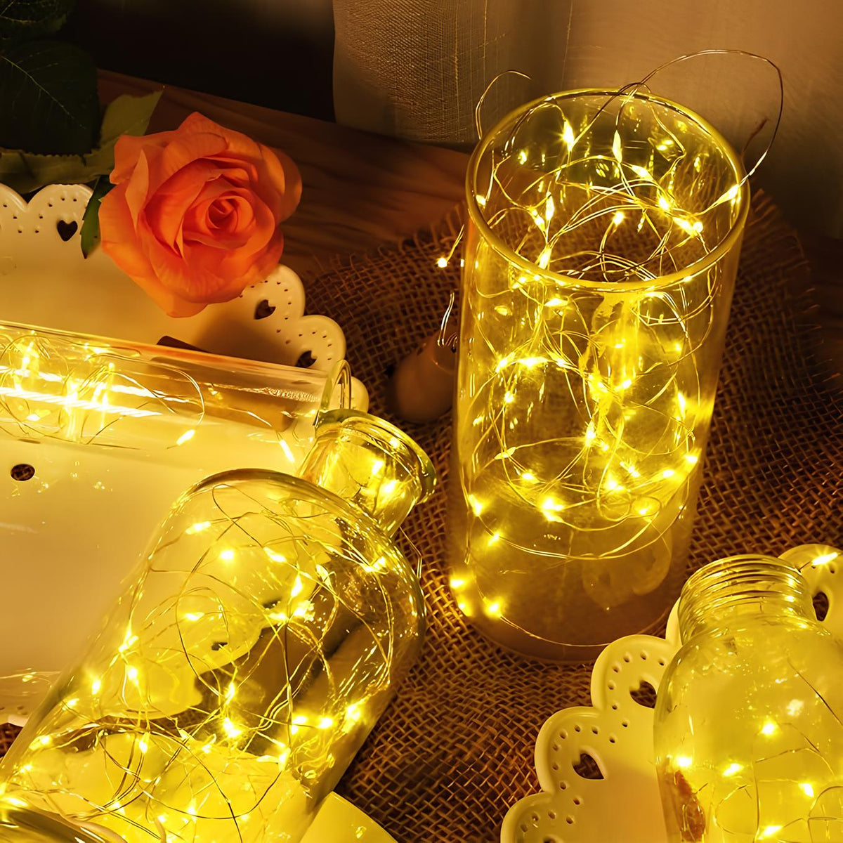 Warm white fairy lights tangled in glass jars and vases beside a rose — Casa Norex