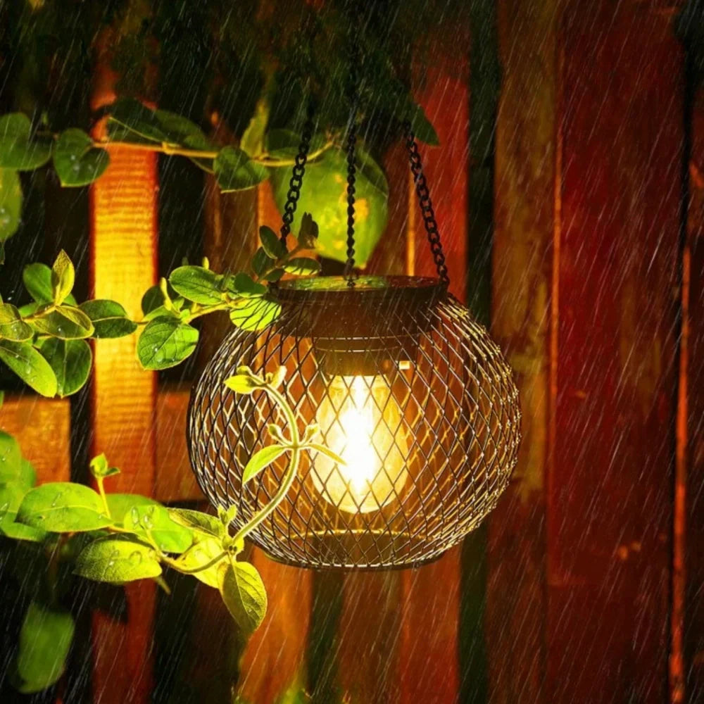 Solar hanging lantern in black metal mesh glowing warm white against a red wall | Casa Norex