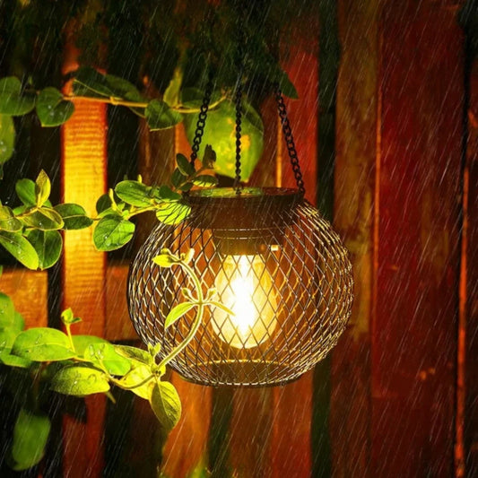 Solar hanging lantern in black metal mesh glowing warm white against a red wall | Casa Norex