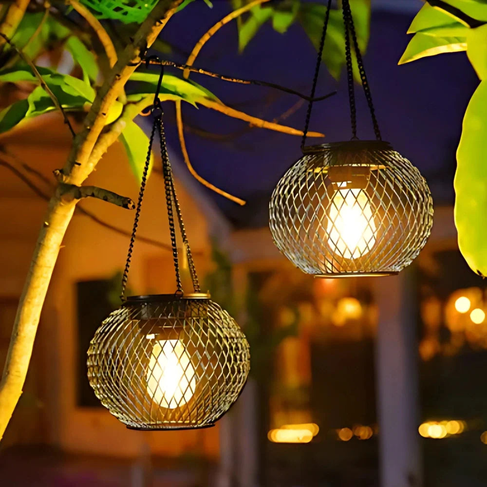 Black mesh solar lanterns hanging from a leafy branch near a patio | Casa Norex