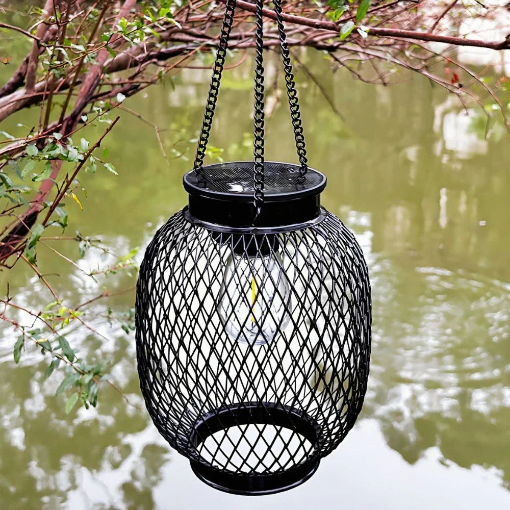 Oval black mesh lantern hanging by a chain over a garden pond — Casa Norex
