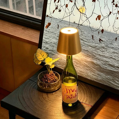 Gold cordless bottle lamp on a bottle by a window with yellow flowers | Casa Norex