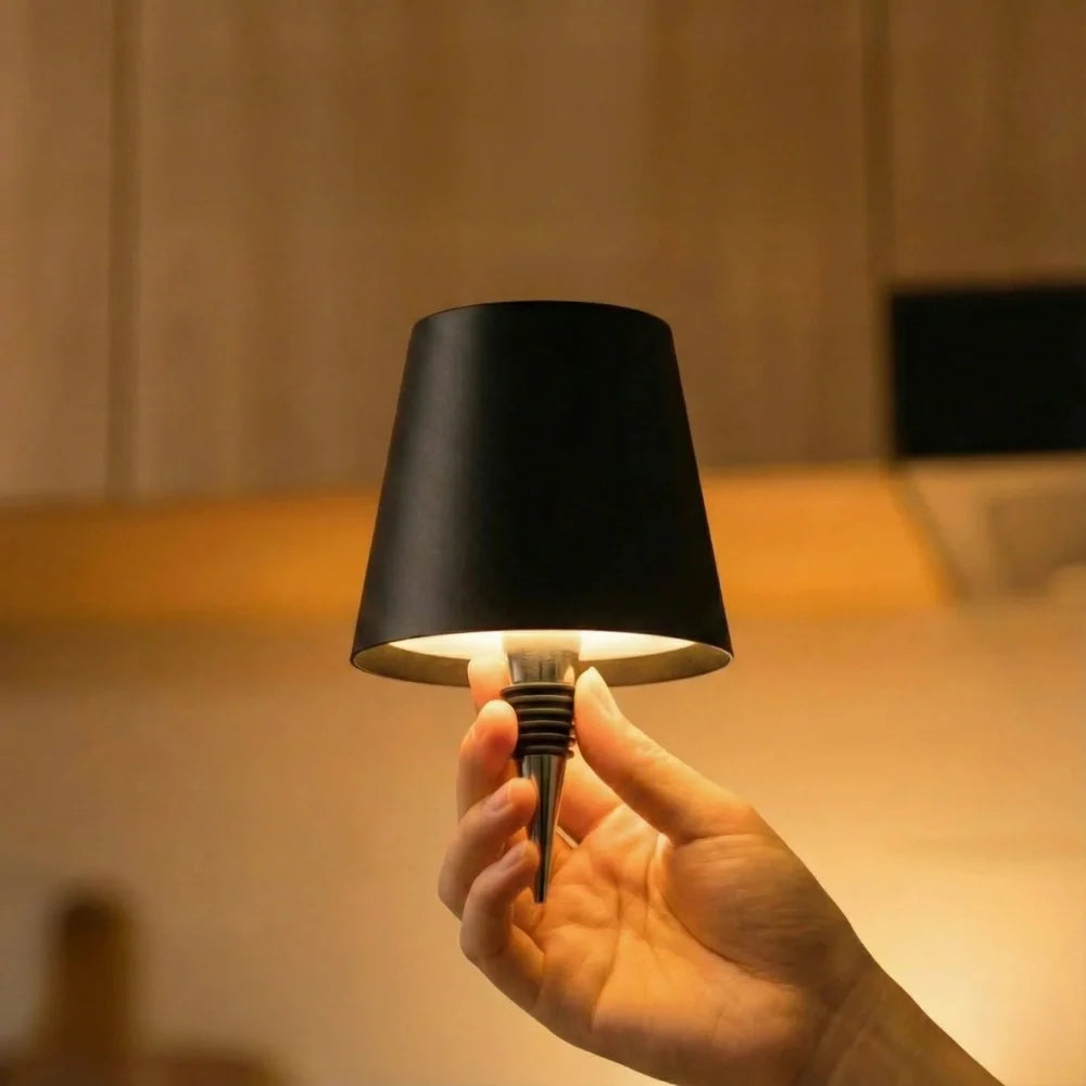 Hand placing a black cordless lamp onto a bottle neck — Casa Norex