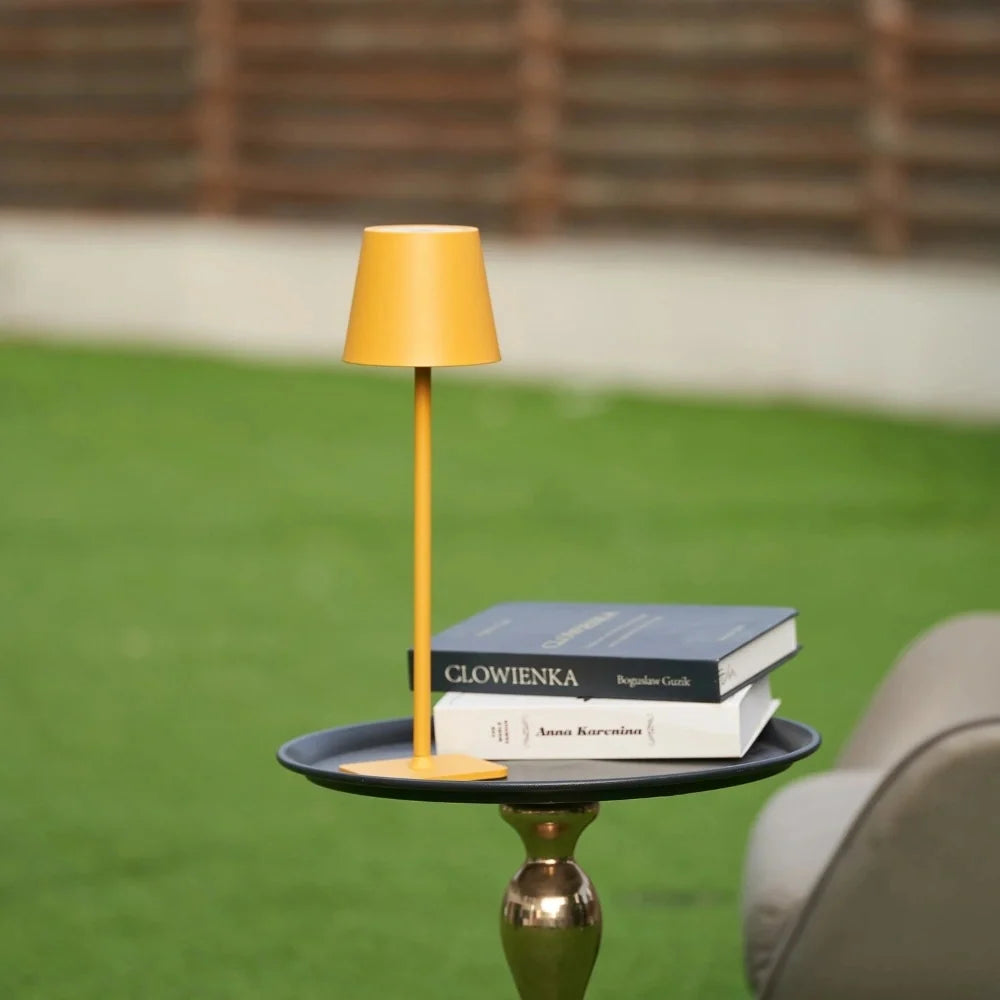 Yellow table lamp on a bronze garden table with books beside it — Casa Norex